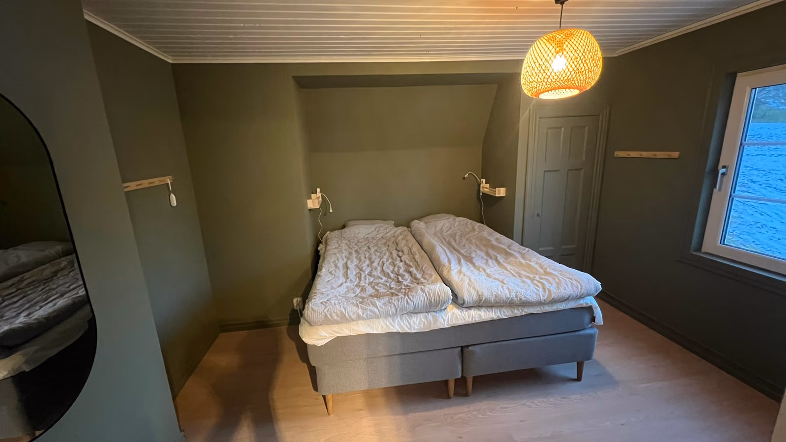 Sovrum med mörkgröna väggar, dubbelsäng under snedtaket och en flätad taklampa